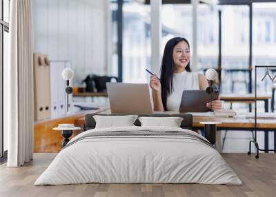 Business asian woman or female worker using a laptop computer to analyse her financial data.business people research or financial strategy in company concept. Laptop white screen mockup. Wall mural