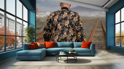 Rear view of a young male in a tiger print jacket walking on the railroad tracks Wall mural