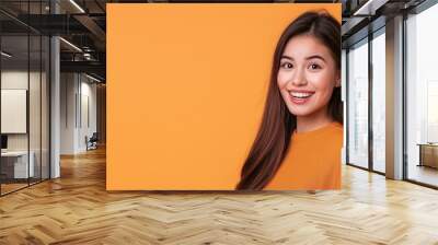 Portrait d'une belle femme eurasienne âgée de 25 ans, heureuse et souriante, isolé sur un fond orange, espace de copie pour texte. Wall mural