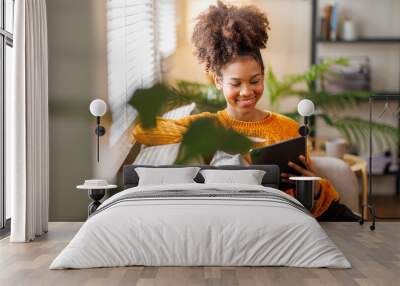 Happy young African American woman using tablet pc on sofa at home. Afro haired woman indoor. Wall mural