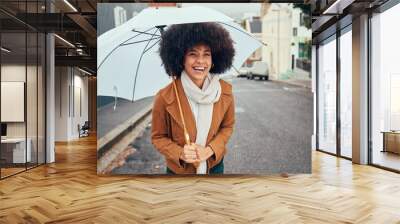 Rain, umbrella and city with a walking black woman in the street during a cold or wet winter day. Water, insurance and cover with a young afro female outdoor for a walk in an urban town road Wall mural