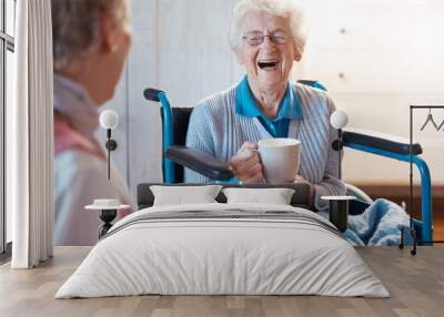 Senior woman, friend and coffee or tea while in a wheelchair for a disability or rehabilitation and happy or laughing about funny conversation or joke. Old people together for fun in nursing home Wall mural