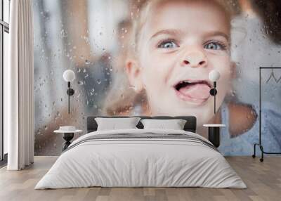 Funny, kid and tongue on window portrait with goofy and enthusiastic face pressed on surface. Young, happy and crazy girl child enjoying playful lick on glass with rain droplets closeup. Wall mural