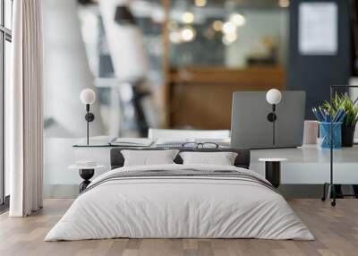 Laptop Computer, notebook, and eyeglasses sitting on a desk in a large open plan office space after working hours	 Wall mural