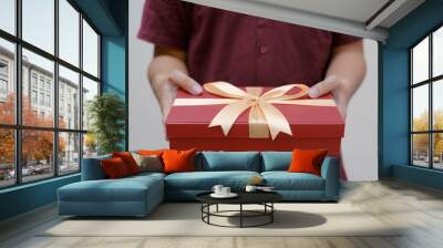 Male hands holding a small red gift box wrapped with gold ribbon. Close up and indoor shot. Selective focus. Christmas Concept. Wall mural