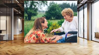 Affectionate young woman talking to elderly woman in a wheelchair in the garden Wall mural