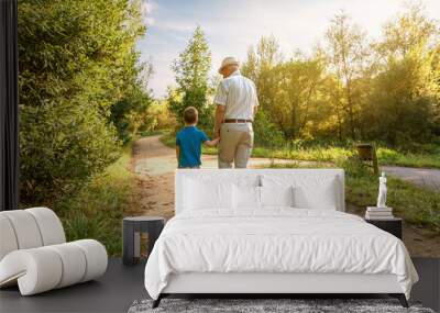 Back view of grandfather with hat and grandchild walking on a nature path Wall mural