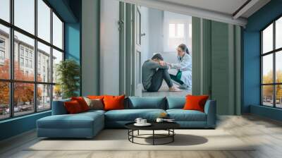 Female doctor reassuring and helping with empathy to male patient sitting on the room floor of a mental health center Wall mural