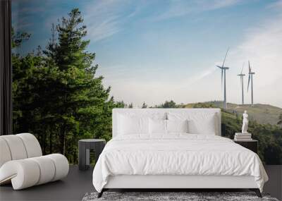 Forest landscape on a sunny day with wind turbines generating electricity in the background. Nature and ecological energy production concept. Wall mural