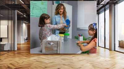 Girl recycling paper with her female teacher in an ecology classroom Wall mural