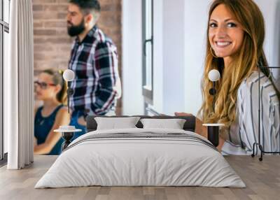 Happy businesswoman looking at camera in office with colleagues in the background Wall mural