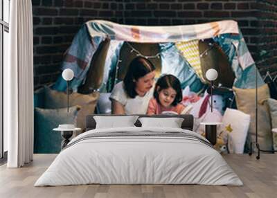 Mother and daughter having a pajama party reading a book in a diy tent Wall mural