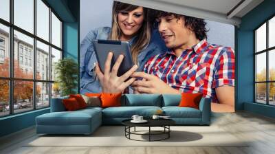 Young couple looking at the tablet sitting on the bed Wall mural