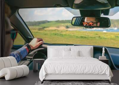 Young man holding steering wheel while driving the car Wall mural