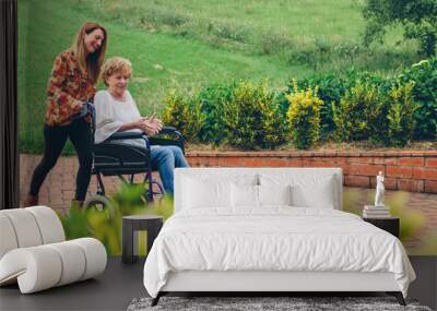 Young woman carrying her mother in a wheelchair through the garden Wall mural