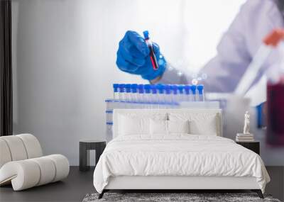 Serious concentrated female microbiologist in sterile clothing and safety goggles sitting at table and dropping reagent in petri dish while doing research in laboratory Wall mural