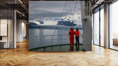 Two persons on the bow of a ship looking over the water at glacier and mountains Wall mural