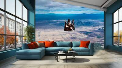 Waving and smiling woman makes skydive alone over Arizona desert with mountains and dramatic clouds Wall mural