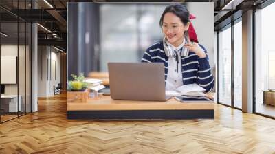 Young adult happy smiling Hispanic Asian student wearing headphones talking on online chat meeting using laptop in university campus or at virtual office. College female student learning remotely.
 Wall mural