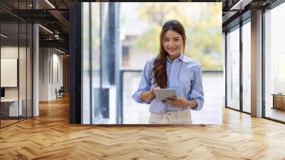 Young business Asian woman using tablet ipad, standing near the window in workplace Wall mural