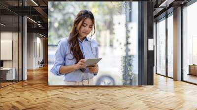 Young business Asian woman using tablet ipad, standing near the window in workplace Wall mural