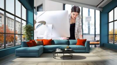 Young happy professional business asian woman employee sitting at desk working on laptop in modern corporate office interior. Smiling female worker using computer technology typing browsing web. Wall mural