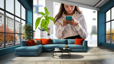 Young woman using smartphone at home. Student girl texting on mobile phone in her room. Communication, home work or study, connection, mobile apps, technology, lifestyle concept Wall mural