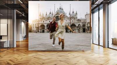 Couple of tourists visiting Venice, Italy - Boyfriend and girlfriend in love running together on city street at sunset - People, love and holidays concept Wall mural