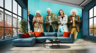 Group of senior people using technology devices together standing on a blue wall - Happy older friends having fun watching funny video on smartphone - Tech and modern elderly concept Wall mural