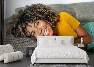 Happy afro american woman relaxing on the sofa at home - Smiling girl taking selfie picture with smartphone lying on the couch - Healthy life style, good vibes people and new home concept Wall mural