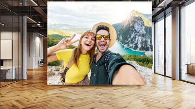 Happy couple taking selfie pic with smart mobile phone on top of the mountain - Young hikers climbing the cliff - Sport, technology and travel life style concept Wall mural