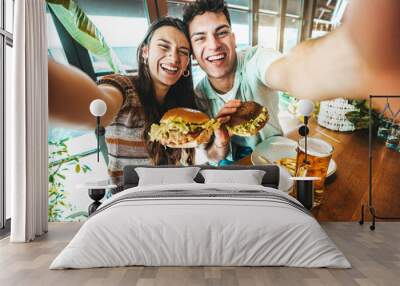 Happy couple taking selfie with smart mobile phone at burger pub restaurant - Young people having lunch break at cafe bar venue - Life style concept with guy and girl hanging out on weekend day Wall mural