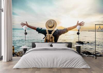 Happy man raising arms up enjoying sunset on the beach - Delightful traveler standing with hands up looking morning sunrise - Self care, traveling, wellness and healthy life style concept Wall mural