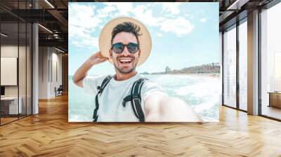 Happy man with hat and sunglasses taking selfie picture with smartphone at the beach  Wall mural