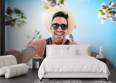 Happy tourist taking self portrait outside with cellphone on summer vacation - Handsome young man laughing at camera enjoying summertime day out - Tourism, traveler life style and technology concept Wall mural