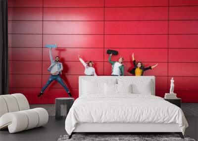 Happy young friends jumping in front of a red wall background - Multiracial teenagers enjoying time together and having fun - Friendship and lifestyle concept Wall mural