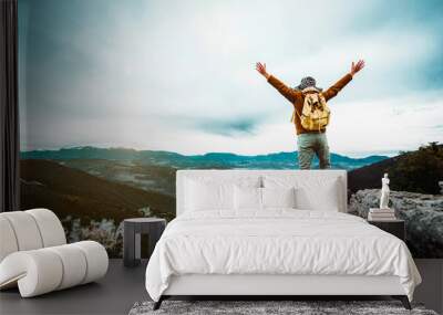 Man standing on edge of mountain feeling victorious with arms up in the air - Hiker triumph success on the top of the cliff - Success, life goals, achievement concept. Wall mural