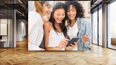 Multiracial young women using smart mobile phone device outside - Happy female friends watching funny video on smartphone - Trendy technology life style concept Wall mural