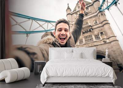 Smiling man taking selfie portrait during travel in London, England - Young tourist male taking holiday pic with iconic england landmark - Happy people wandering around Europe concept Wall mural