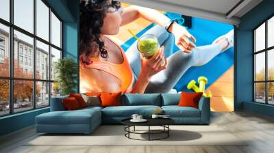 Sporty woman in sportswear training at home drinking fresh smoothie - Fit female athlete using smart watch to monitor her performance - Sport, food and technology concept Wall mural