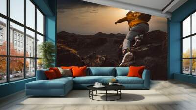 Successful hiker hiking a mountain pointing to the sunset. Wild man with backpack climbing a rock over the storm. Success, wanderlust and sport concept. Wall mural