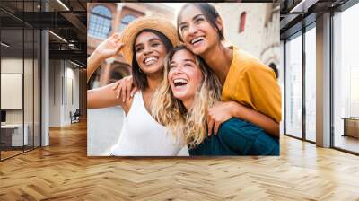 Three young multiracial women having fun on city street outdoors - Mixed race female friends enjoying a holiday day out together - Happy lifestyle, youth and young females concept Wall mural