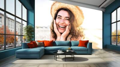 Young joyful woman in white shirt wearing hat smiling at camera on the beach - Traveler girl enjoying freedom outdoors on a sunny day - Wellbeing, healthy lifestyle and happy people concept Wall mural