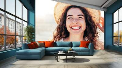 Young joyful woman in white shirt wearing hat smiling at camera on the beach - Traveler girl enjoying freedom outdoors on a sunny day - Wellbeing, healthy lifestyle and happy people concept Wall mural