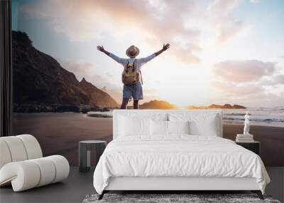 Young man arms outstretched by the sea at sunrise enjoying freedom and life, people travel wellbeing concept Wall mural