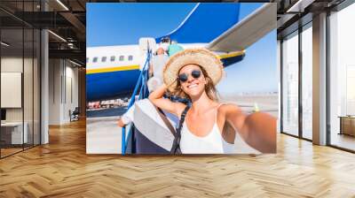 Young woman takes a selfie at the airport in front of a plane before the departure. Concept about travel and technology Wall mural