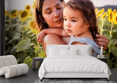 young mother and baby toddler daughter hugging and playing together outdoors in a sunflowers field in the nature. Concept of family quality time and bonding Wall mural