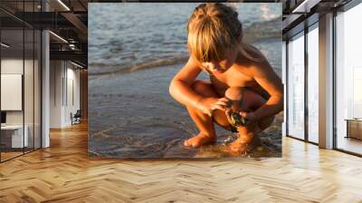 Caucasian blonde little girl playing with sand on the beach at sunset Wall mural