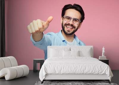 Portrait of trendy young bearded man in blue stylish shirt and eyeglasses showing thumb up over pink background Wall mural