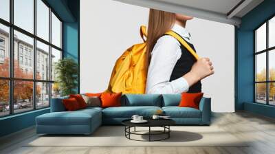 Vertical photo of side view schoolgirl with yellow backpack smiling and looking at camera while against white background. Back to school concept Wall mural